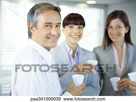Business colleagues standing in office with cups in hands, smiling at camera View Large Photo Image Stock Photo - Business colleagues standing in office with cups in hands, smiling at camera. Fotosearch
