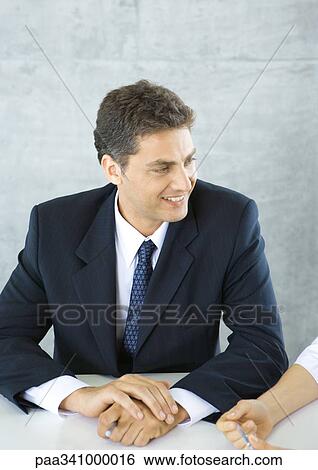 Businessman sitting at table, smiling at colleague View Large Photo Image Stock Photograph - Businessman sitting at table, smiling at colleague. Fotosearch