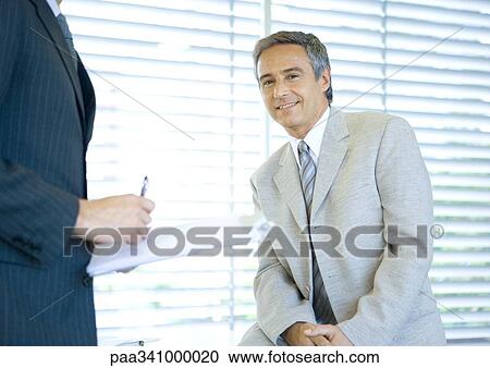 Stock Image - Businessman smiling at camera while colleague signs document. Fotosearch