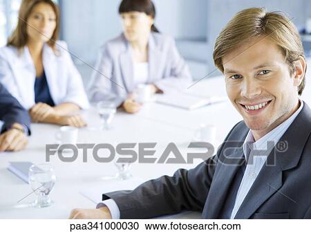 Businessman smiling, meeting in background, portrait View Large Photo Image Stock Image - Businessman smiling, meeting in background, portrait. Fotosearch
