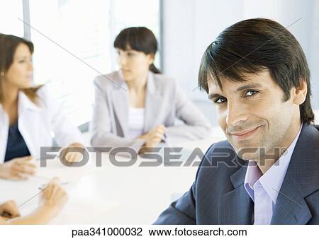 Businessman smiling, meeting in background, portrait View Large Photo Image Stock Image - Businessman smiling, meeting in background, portrait. Fotosearch
