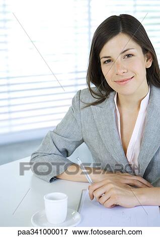 Businesswoman sitting at table with pen and cup of coffee, smiling at camera View Large Photo Image Stock Photo - Businesswoman sitting at table with pen and cup of coffee, smiling at camera. Fotosearch