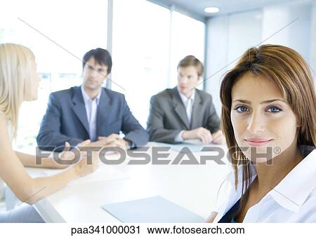 Businesswoman smiling at camera, meeting in background, portrait View Large Photo Image Stock Image - Businesswoman smiling at camera, meeting in background, portrait. Fotosearch