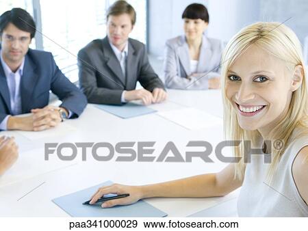 Stock Photo - Businesswoman smiling at camera, meeting in background, portrait. Fotosearch