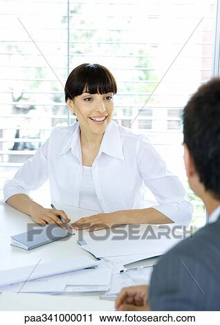 Stock Image - Businesswoman talking to colleague across table. Fotosearch
