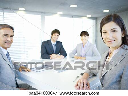 Executives sitting around table, smiling at camera View Large Photo Image Stock Photo - Executives sitting around table, smiling at camera. Fotosearch