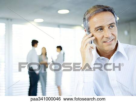 Mature businessman using cell phone, colleagues talking in background View Large Photo Image Stock Photograph - Mature businessman using cell phone, colleagues talking in background. Fotosearch