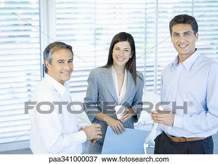 Three business colleagues standing in office with cups in hands, smiling at camera View Large Photo Image Stock Photo - Three business colleagues standing in office with cups in hands, smiling at camera. Fotosearch