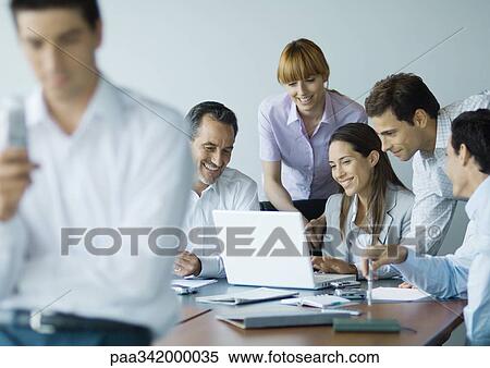 Business colleagues gathered around laptop, smiling View Large Photo Image Stock Photography - Business colleagues gathered around laptop, smiling. Fotosearch