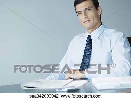 Stock Image - Businessman sitting at desk, portrait. Fotosearch