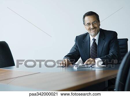 Stock Image - Mature businessman sitting at conference table. Fotosearch