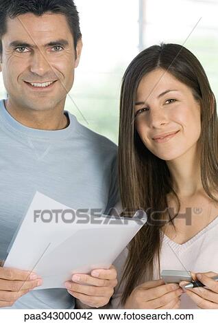 Stock Image - Couple holding document and calculator, smiling at camera. Fotosearch