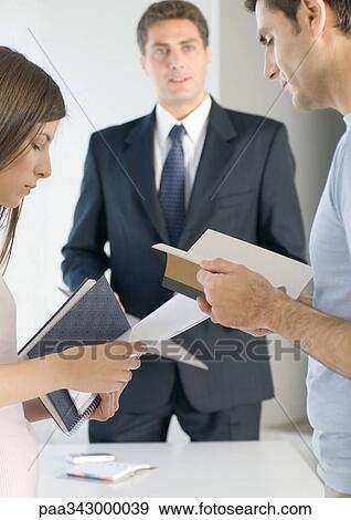 Couple looking at literature while sales executive stands in background View Large Photo Image Stock Photo - Couple looking at literature while sales executive stands in background. Fotosearch