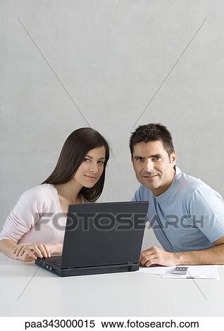 Couple using laptop, smiling at camera View Large Photo Image Stock Photography - Couple using laptop, smiling at camera. Fotosearch