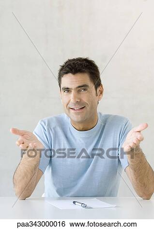Man sitting with paper and pen, gesturing toward camera View Large Photo Image Stock Photograph - Man sitting with paper and pen, gesturing toward camera. Fotosearch