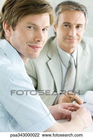 Stock Image - Young man with mature business man, smiling at camera. Fotosearch