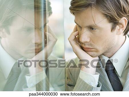 Stock Image - Businessman holding head, face reflected in window. Fotosearch