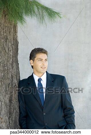 Stock Image - Businessman leaning against tree, portrait. Fotosearch