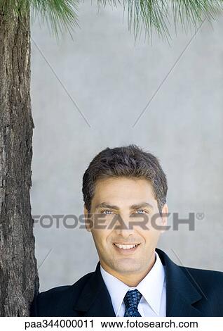 Stock Image - Businessman next to tree, portrait. Fotosearch
