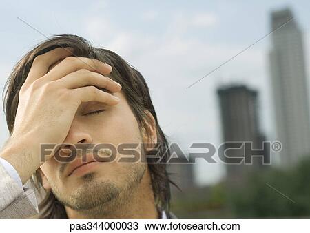 Stock Image - Young businessman holding head and closing eyes. Fotosearch