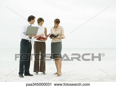 Stock Image - Business team consulting agendas on beach. Fotosearch