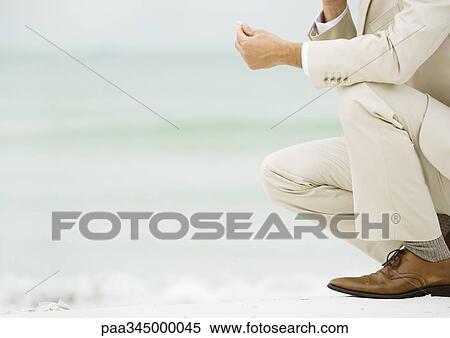 Businessman crouching on beach, holding something in fingers View Large Photo Image Stock Photography - Businessman crouching on beach, holding something in fingers. Fotosearch