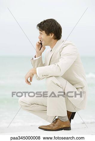 Businessman crouching on beach, using cell phone View Large Photo Image Stock Photo - Businessman crouching on beach, using cell phone. Fotosearch