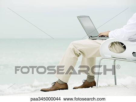Businessman sitting in chair, using laptop on beach, waist down View Large Photo Image Picture - Businessman sitting in chair, using laptop on beach, waist down. Fotosearch