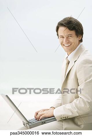 Businessman using laptop, smiling at camera View Large Photo Image Stock Photograph - Businessman using laptop, smiling at camera. Fotosearch