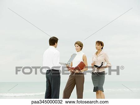 Businessman with laptop facing women with agendas, on beach View Large Photo Image Stock Image - Businessman with laptop facing women with agendas, on beach. Fotosearch