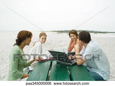 Four casually dressed adults sitting at picnic table on beach, with laptop and agendas View Large Photo Image Stock Photograph - Four casually dressed adults sitting at picnic table on beach, with laptop and agendas. Fotosearch