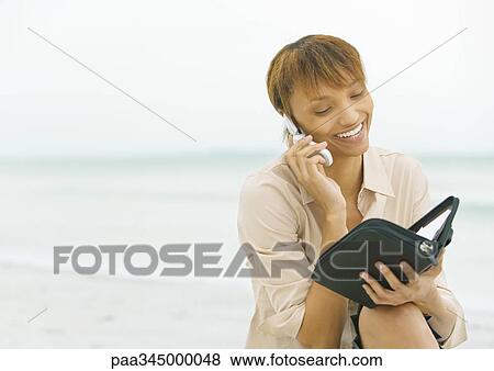 Woman on beach, using cell phone and looking at agenda View Large Photo Image Stock Photo - Woman on beach, using cell phone and looking at agenda. Fotosearch