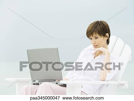 Stock Photo - Woman sitting in deckchair using laptop. Fotosearch