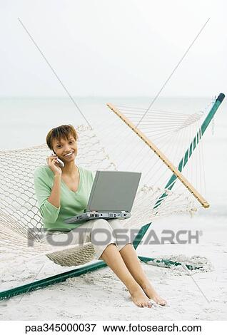 Woman sitting on hammock on beach, using cell phone and laptop View Large Photo Image Stock Photo - Woman sitting on hammock on beach, using cell phone and laptop. Fotosearch