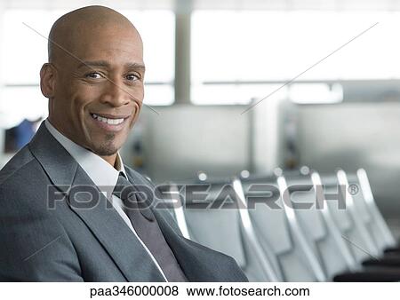 Businessman sitting in airport lounge, smiling at camera View Large Photo Image Stock Photo - Businessman sitting in airport lounge, smiling at camera. Fotosearch