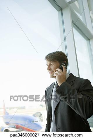 Stock Photo - Businessman using cell phone by window in airport. Fotosearch
