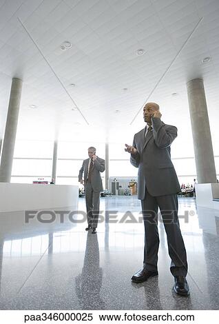 Businessmen using cell phones in airport concourse View Large Photo Image Stock Photography - Businessmen using cell phones in airport concourse. Fotosearch