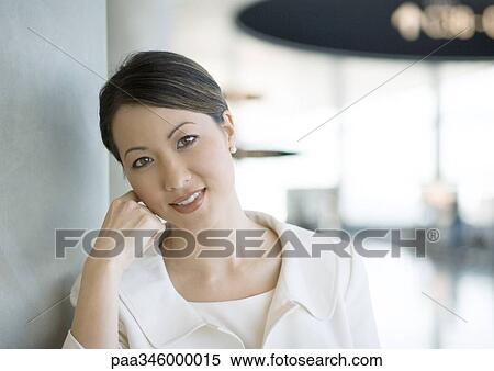 Stock Photography - Female traveler leaning head on hand in airport, smiling at camera. Fotosearch