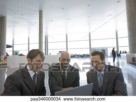 Three businessmen using laptop in airport View Large Photo Image Picture - Three businessmen using laptop in airport. Fotosearch