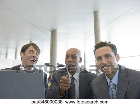 Three businessmen with laptop, smiling and pointing at camera View Large Photo Image Stock Photo - Three businessmen with laptop, smiling and pointing at camera. Fotosearch