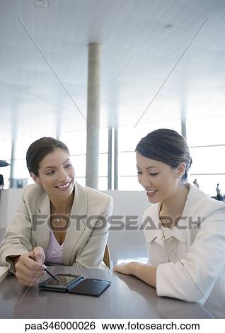 Two businesswomen using electronic organizer View Large Photo Image Stock Photograph - Two businesswomen using electronic organizer. Fotosearch
