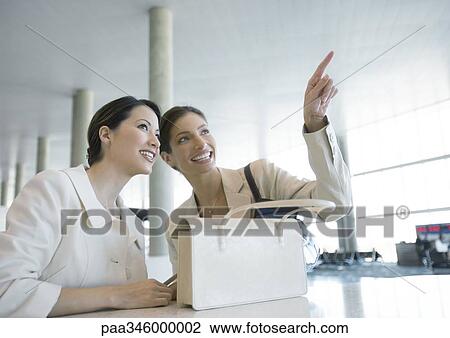 Two women in airport, one pointing View Large Photo Image Stock Image - Two women in airport, one pointing. Fotosearch