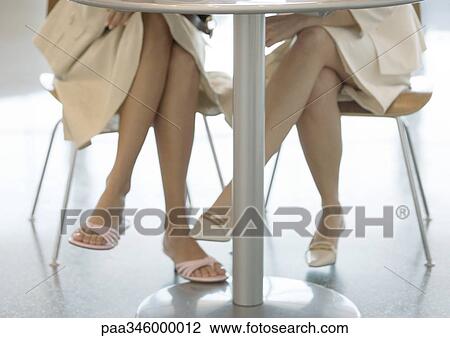Two women sitting at table, view of legs under table View Large Photo Image Stock Image - Two women sitting at table, view of legs under table. Fotosearch