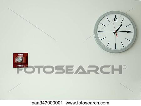 Stock Image - Clock and fire alarm on wall. Fotosearch