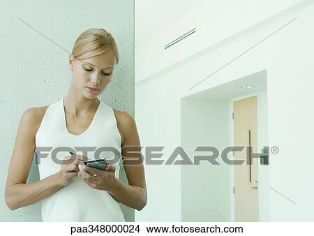Picture - Woman using electronic organizer in hallway of office building. Fotosearch