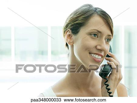 Stock Image - Woman using telephone, smiling. Fotosearch