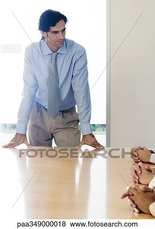 Stock Photo - Businessman standing with hands on table during meeting. Fotosearch