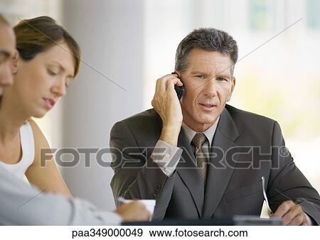 Businessman using cell phone, sitting near colleagues View Large Photo Image Stock Photo - Businessman using cell phone, sitting near colleagues. Fotosearch