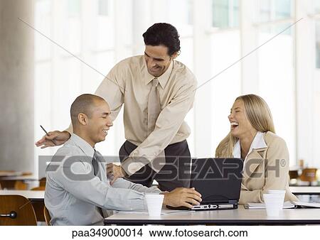 Group of young executives laughing, one man standing and tapping second man on the back View Large Photo Image Picture - Group of young executives laughing, one man standing and tapping second man on the back. Fotosearch