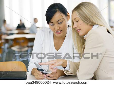 Two young business women looking at cell phone together View Large Photo Image Picture - Two young business women looking at cell phone together. Fotosearch